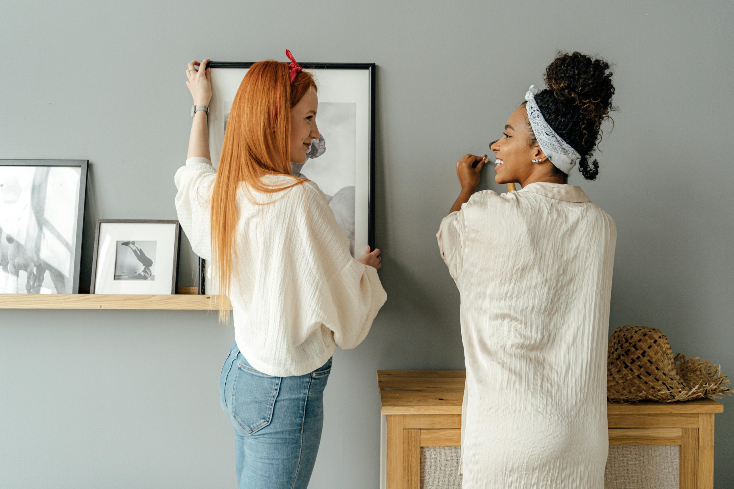 Two women hang pictures on a wall, showcasing home decor and friendship.